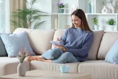 Evdeki kanepede oturan mavi elbiseli mutlu bir kadın.