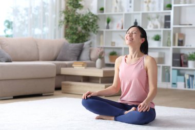 Mutlu Asyalı kadın evde halıda nefes egzersizi yapıyor.