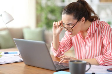 Kötü gözlüklü serbest meslek görme zoruyla evdeki laptop ekranından içeriği okumaya çalışıyor.