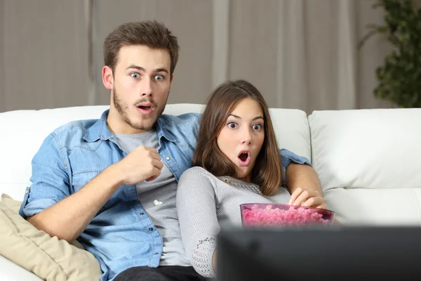 Pareja asombrada viendo la televisión en casa — Foto de Stock