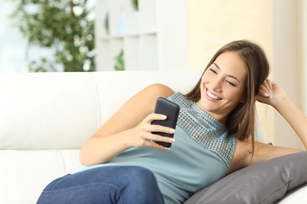 Dona de casa feliz usando um telefone celular em um sofá — Fotografia de Stock