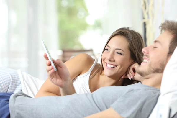 Pasangan berbagi ponsel pintar di tempat tidur — Stok Foto