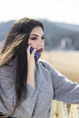 Güzel genç kız kumsalın yakınında telefonla konuşuyor, uzun saçlı ve gri elbiseli.