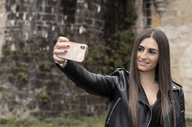 Deri elbiseli genç bir kadın kalenin önünde selfie çekiyor.