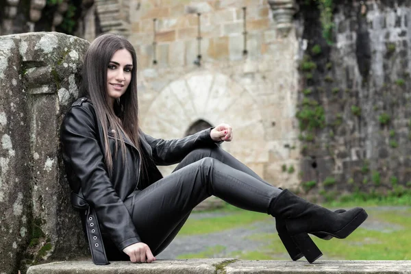 Eski bir şatonun önünde deri ceket giymiş güzel esmer bir kadının portresi.