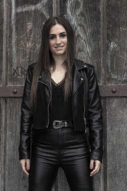 Genç esmer kadın deri giysiler içinde yürüyor.