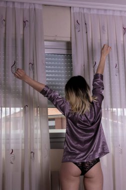 İç çamaşırlı kadın pencerenin önünde geriniyor.