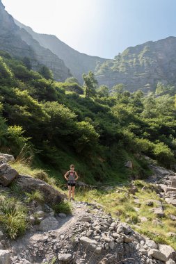 Güneş gözlüklü esmer kadın çalıların arasında kolları ve şortlarıyla yürüyor.