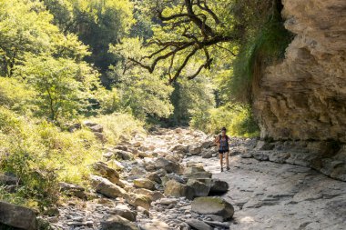 Ormanda yürüyen bir kadın kayalık kanyonu geçerek kameraya yaklaşıyor.