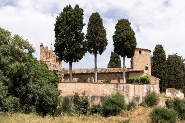 Peratallada, spain, showing ancient stone architecture and tall cypress trees under a cloudy sky