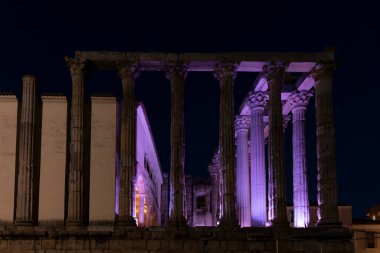 Mor ışıklarla aydınlatılmış antik Roma tapınağı sütunları derin mavi bir gökyüzüne karşı