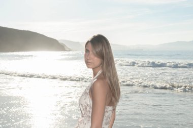 Güneş suyu yansıtırken sahilde huzurlu bir yürüyüşün tadını çıkaran bir kadın.