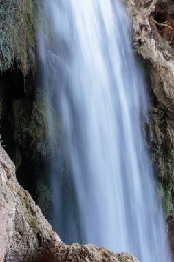 Şelale akıntısı uzun pozlama tekniğini kullanarak yemyeşil yosun ile kahverengi kayaların üzerinden akıyor.