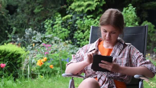 Jovem mulher lendo e-book no jardim — Vídeo de Stock