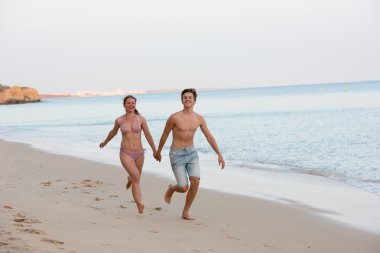 Genç bir çift sahilde koşuyor. 