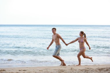 Genç bir çift sahilde koşuyor. 