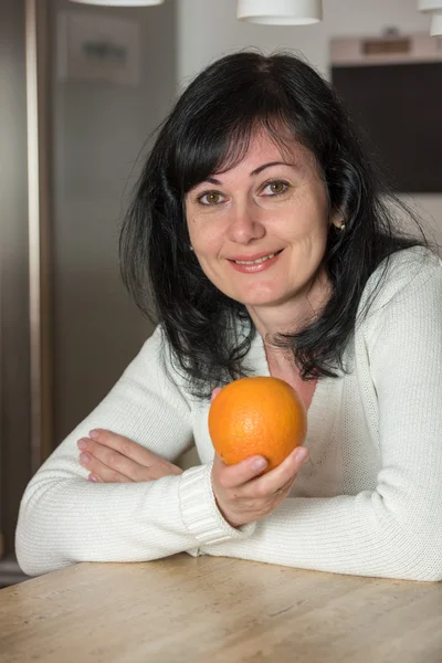 Woman in the kitchen with an orange — Stock Photo, Image