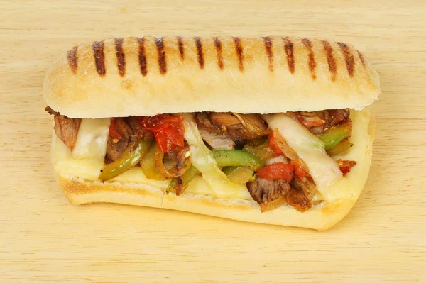 Biftek, soğan, biber, domates ve ahşap kesim tahtasındaki panini içinde emmental peynir.