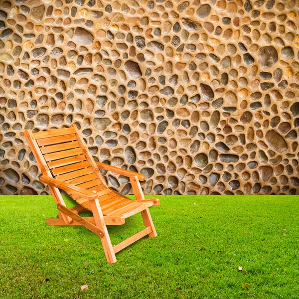 wooden deck chair on green grass with stone wall background