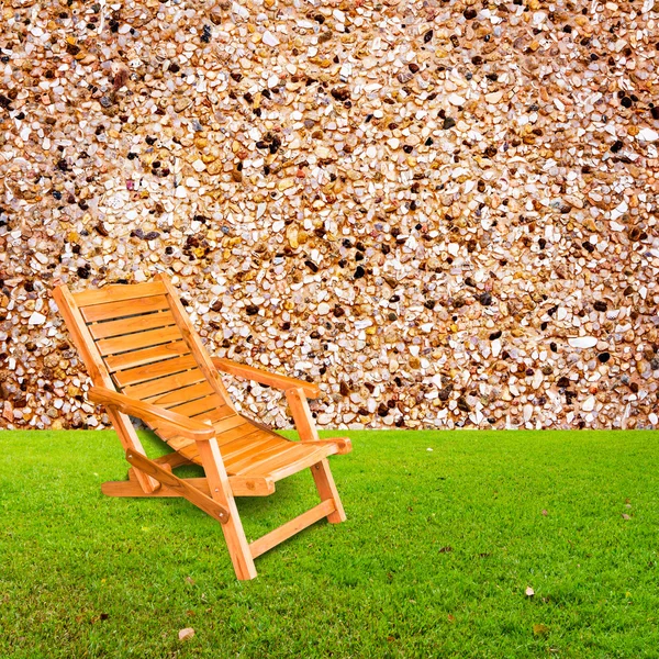 Dřevěné lehátko na zelené trávě s kamennou zeď pozadí — Stock fotografie