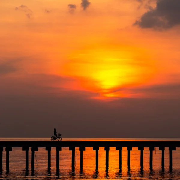 Silhueta menino passeio de bicicleta na ponte ao pôr do sol — Fotografia de Stock