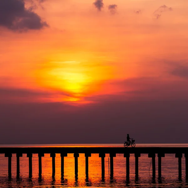 Silhueta menino passeio de bicicleta na ponte ao pôr do sol — Fotografia de Stock