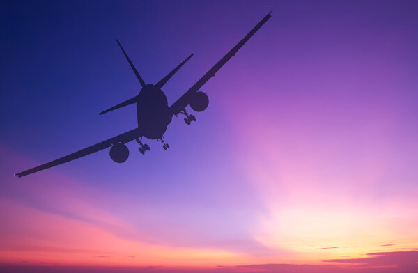 Silhouetted commercial airplane flying at sunset