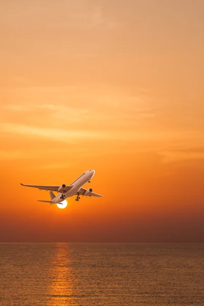 सूर्यास्त पर समुद्र के ऊपर उड़ान भरने वाले वाणिज्यिक विमान — स्टॉक फ़ोटो, इमेज