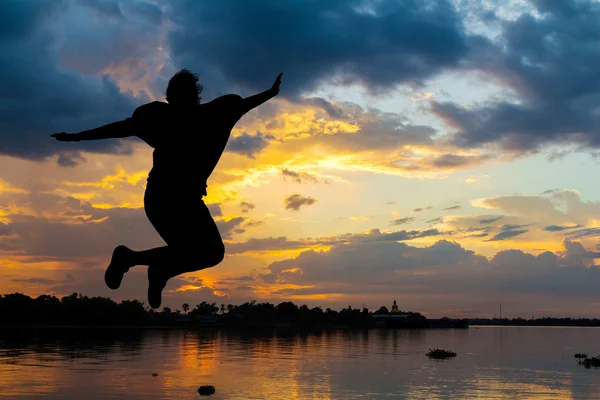 Senhora saltando feliz ao lado do rio ao pôr do sol — Fotografia de Stock