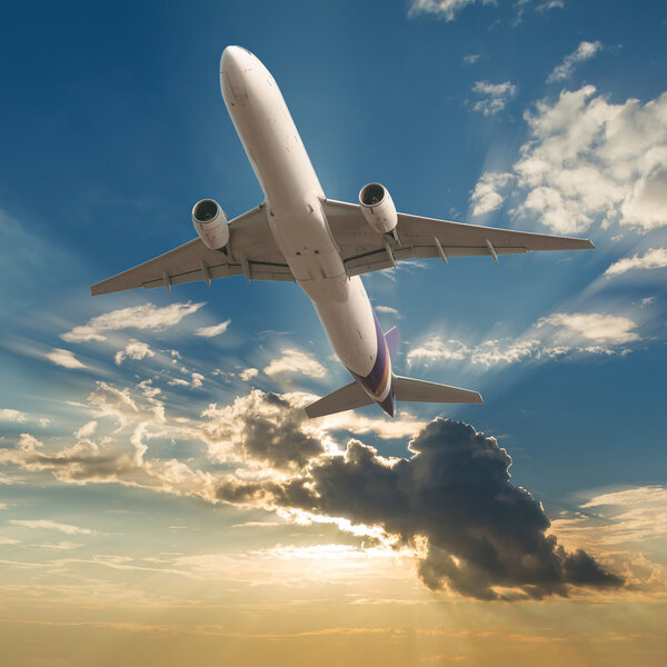 Commercial airplane flying with clouds and sun rays background