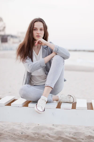 Μοντέρνα πορτρέτο ενός κοριτσιού που θέτουν στην παραλία το ηλιοβασίλεμα σε ένα κομψό άνετα ρούχα. Νεαρή γυναίκα σε εξωτερικούς χώρους — Φωτογραφία Αρχείου