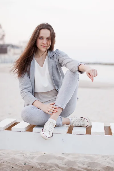 Fashionabla porträtt av en flicka som poserar på stranden vid solnedgången i en snygg bekväma kläder. Ung kvinna utomhus — Stockfoto