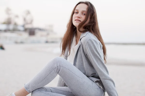 Fashionabla porträtt av en flicka som poserar på stranden vid solnedgången i en snygg bekväma kläder. Ung kvinna utomhus — Stockfoto