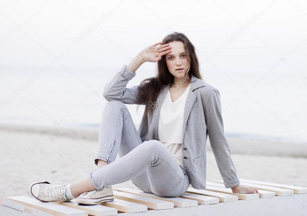 Fashionable portrait of a girl posing on the beach at sunset in a stylish comfortable clothing. Young woman outdoors