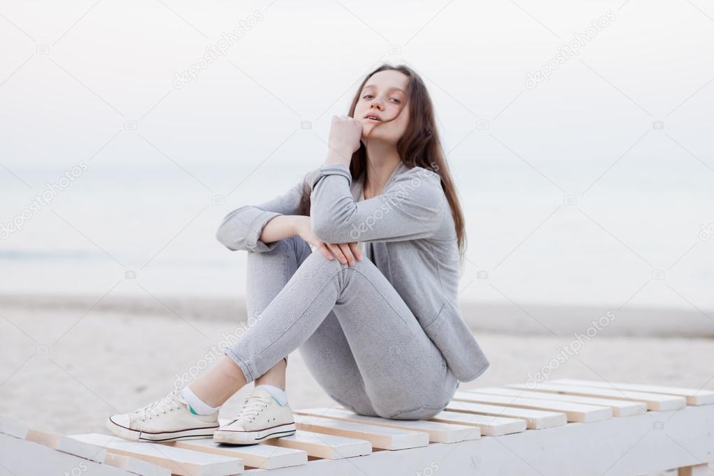 Fashionable portrait of a girl posing on the beach at sunset in a stylish comfortable clothing. Young woman outdoors