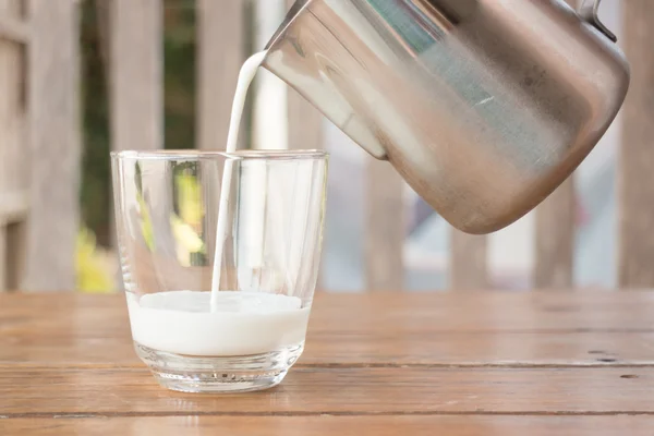 Pour milk from a pitcher into a glass — Stock Photo, Image