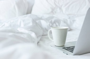 Beyaz yataktaki bilgisayarda bir fincan kahve. Mola zamanı.