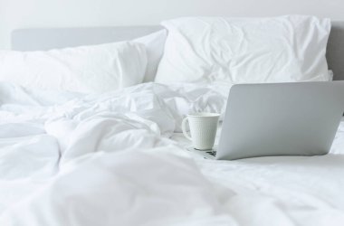 Beyaz yataktaki bilgisayarda bir fincan kahve. Mola zamanı.