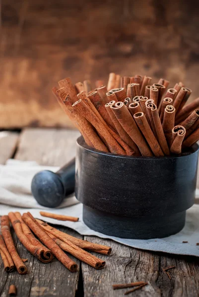 Paus de canela em uma argamassa de pedra na mesa de madeira — Fotografia de Stock