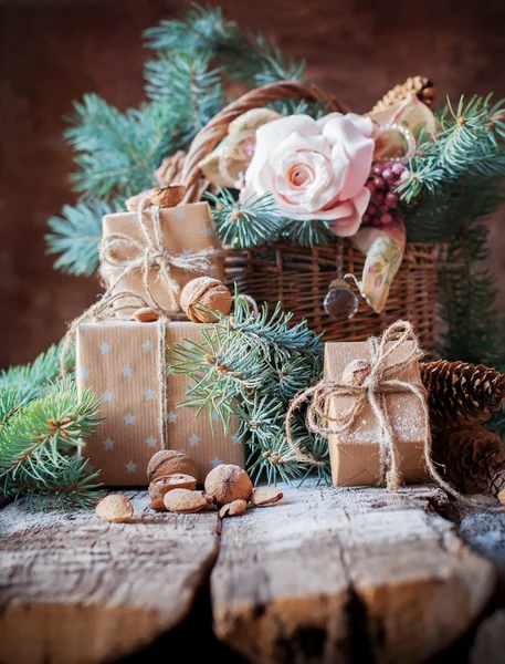 Рождественский натюрморт с подарками в винтажном стиле. Коробки, корд, корзина, хвойные, еловые игрушки, орехи, миндаль на деревянном фоне — стоковое фото