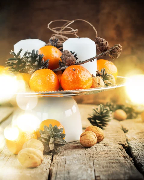 Festtafel mit Mandarinen, Tannenzapfen, Walnüssen, Kerzen auf Holzgrund. Weihnachtslicht — Stockfoto