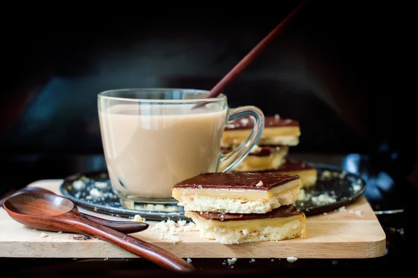 Milchtee mit Schokolade-Karamell-Keksen auf schwarzem Hintergrund — Stockfoto