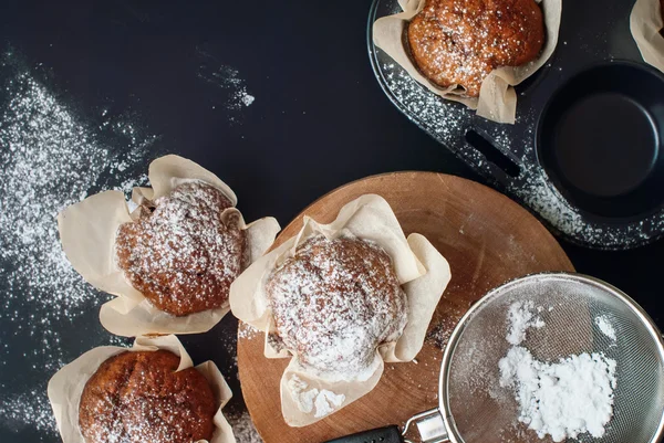 Fresh muffins, sprinkle with powdered sugar, on black table — Stock Photo, Image