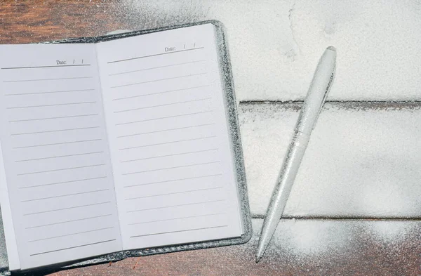 The notebook lies on a dark wooden background dusted with snow