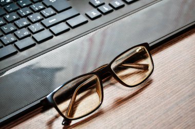 Ofis masasında doğal arka planı olan klavye ve gözlük..
