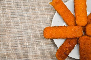 Beyaz bir tabakta kızarmış balık, gri bir hasır arka planda.