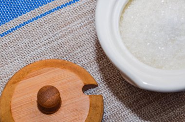 Seramik beyaz şeker kasesi, ahşap kapaklı, gri bir hasır zemin üzerinde şeker