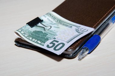 Sarmal, otomatik kalem ve ahşap masadaki 50 dolarlık banknotlar üzerine açık boş defterin üst görünümü.