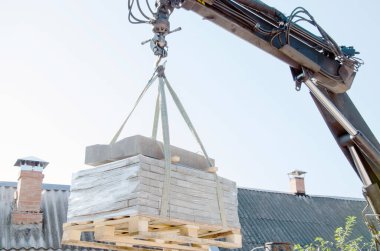 Kamyondan kaldırım levhaları indiriyorum. Erkekler kaldırım levhalarını manipülatör kullanarak boşaltır. İşçiler inşaat malzemelerini büyük bir makineden boşaltıyorlar.