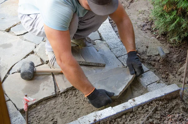 Evin yakınında asfalt inşaatı. Tuğlacı kaldırım inşaatı için beton kaldırım taşı blokları yerleştirdi